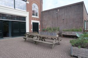 Houten picknicktafels en plantenbakken op een binnenplaats bij het Gedempt Hamerkanaal.